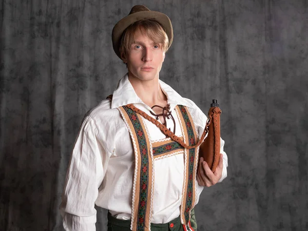 A young man in a national Bavarian suit with shorts on suspenders and a hat. — Stock Photo, Image