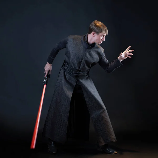 A villain with a red lightsaber, a young man in a long robe does fighting poses, — Stock Photo, Image
