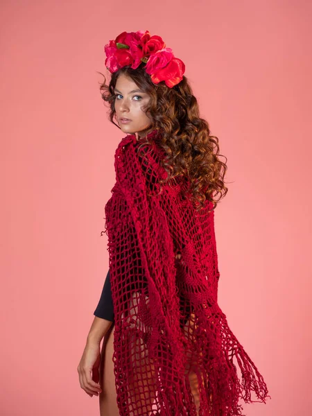 En ljus och djärv ung kvinna med rosor på huvudet och en röd stickad mantel. — Stockfoto