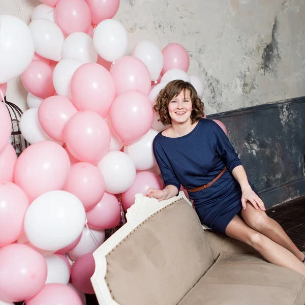 Mujer joven en el sofá en una habitación llena de globos inflables —  Fotos de Stock