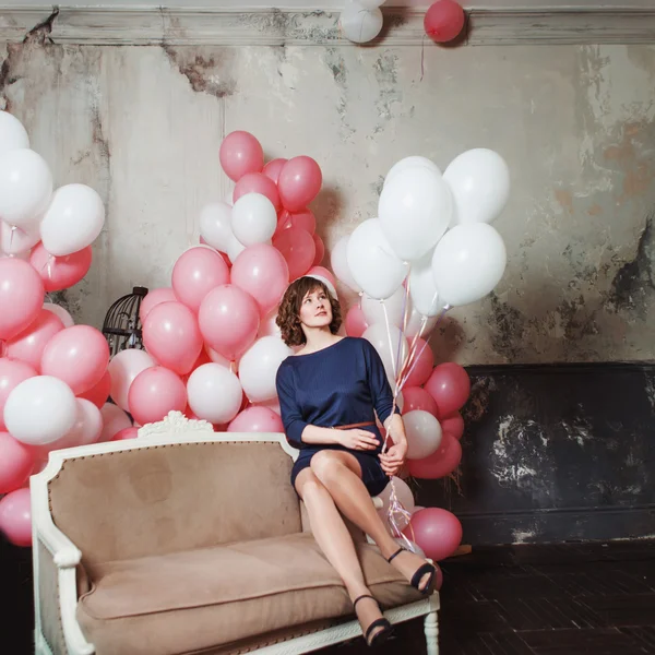 Молодая женщина на диване в комнате, полной надувных шариков — стоковое фото