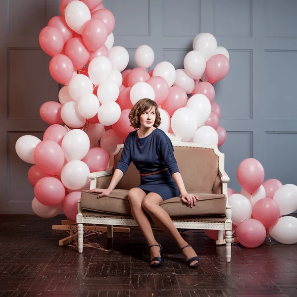 Молода жінка сидить на дивані в кімнаті, повній надувних кульок — стокове фото