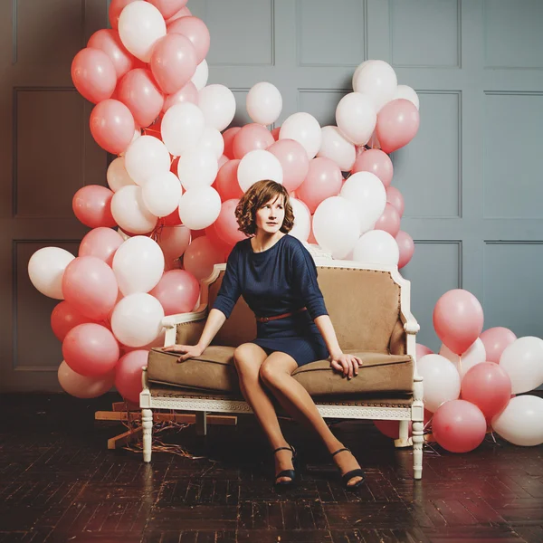 Jonge vrouw op de Bank in een kamer vol van Luchtballons Opblaasbare, warm toning — Stockfoto