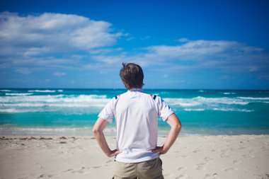 Handsome young man  against bright beach background, looking at the ocean