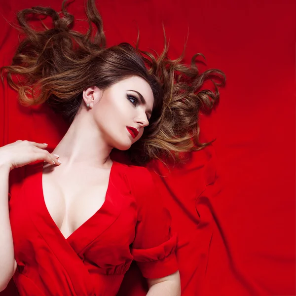 Жінка в сукні лежить на червоному тлі, виглядає правильно — стокове фото