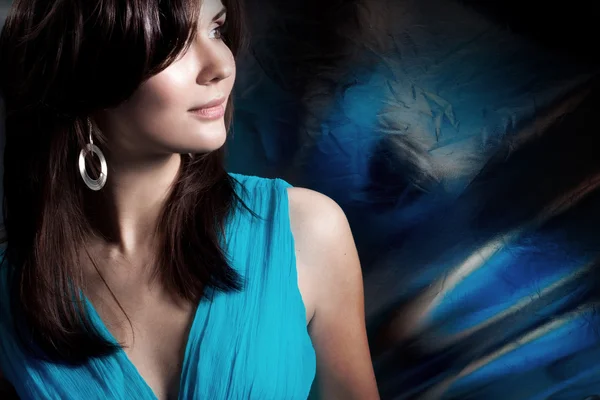 Hermosa mujer de pelo largo en un vestido azul sobre fondo oscuro — Foto de Stock