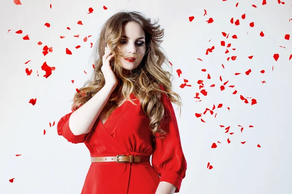 Gül yaprakları arasında Kırmızı elbiseli genç muhteşem kadın moda fotoğrafı — Stok fotoğraf