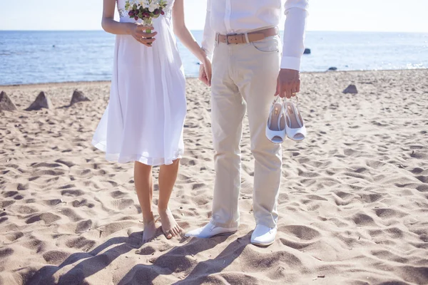 Casamento apenas casal correndo em uma praia de areia, pés vista, noivo detém sapatos — Fotografia de Stock