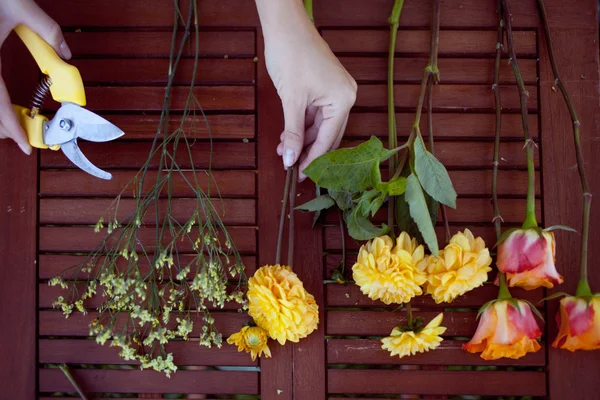 Fleurs et outils sur la table, lieu de travail fleuriste, nature morte vue de dessus — Photo