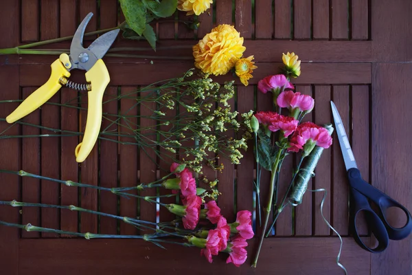 Fleurs et outils sur la table, lieu de travail fleuriste, nature morte vue de dessus — Photo