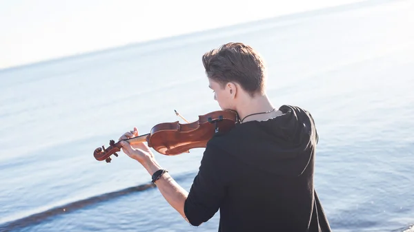 Violinist playing a violin,  young man plays on the background of  sea, back in  frame — Stock Photo, Image