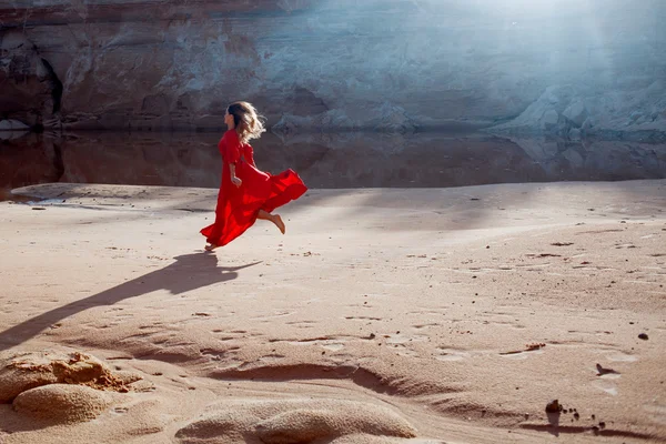 Mulher de vestido vermelho acenando com tecido voador corre no fundo da carreira areias — Fotografia de Stock