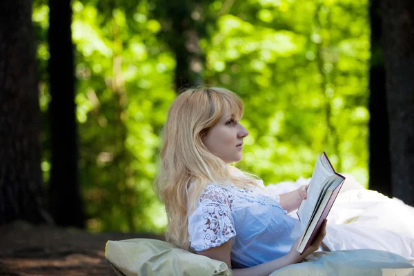 Young beautiful girl woke up  in bed among the woods, and reading a book, conceptual image — Stock Photo, Image