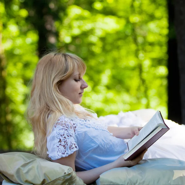 Jovem menina bonita acordou na cama entre a floresta, e lendo um livro, imagem conceitual — Fotografia de Stock