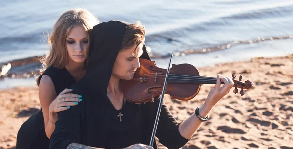 Violist en zijn muze, jonge man speelt op de achtergrond van de zee — Stockfoto