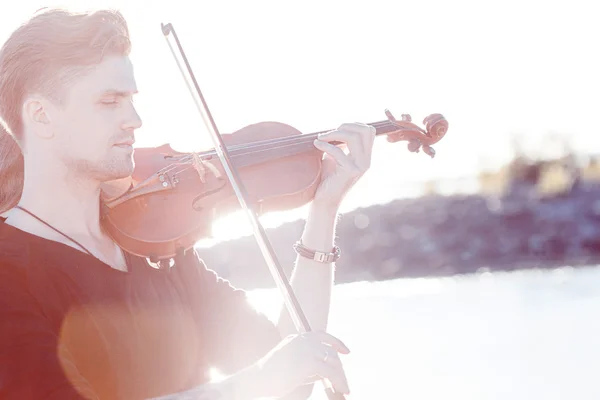 Violist spelen een viool, jonge man speelt op de achtergrond van de zee, zonne-verven — Stockfoto