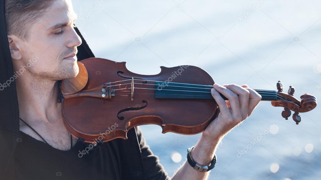 Violinist playing a violin,  young man plays on the background of  sea
