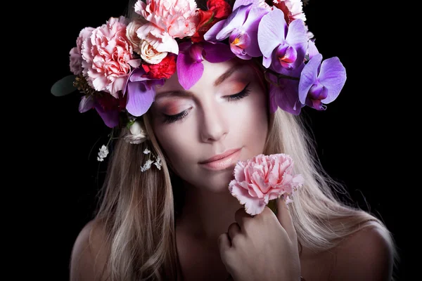 Young beautiful woman in wreath of flowers presses flower to her lips, black background — Stock Photo, Image