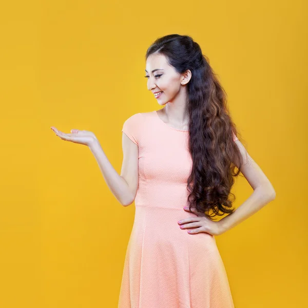 Азиатская молодая девушка держит что-то в руке, место для вашего сообщения. Портрет на желтом фоне . — стоковое фото