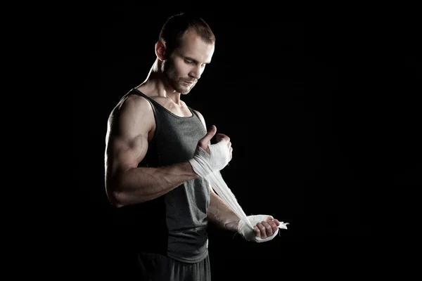 Muscular man, tying an elastic bandage on his hand, black background — Stock Photo, Image