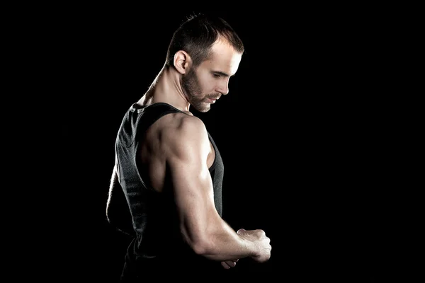 Muscular man,  clasps hands in  fist, black background, place for text on the right — Stock Photo, Image