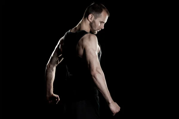 Muscular man,  clasps hands in  fist, black background, place for text on the right — Stock Photo, Image