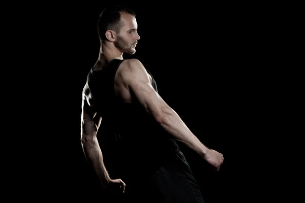 Muscular man,  clasps hands in  fist, black background, place for text on the right — Stock Photo, Image