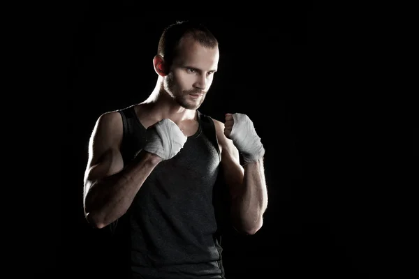 Muscular man, tying an elastic bandage on his hand, black background — Stock Photo, Image