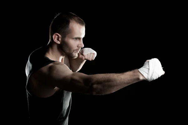 Muscular man, tying an elastic bandage on his hand, black background — Stock Photo, Image