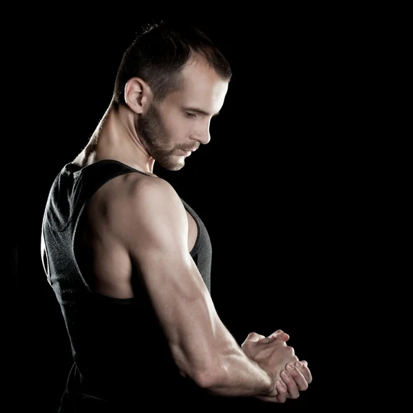 Muscular man,  clasps hands in  fist, black background, place for text on the right — Stock Photo, Image