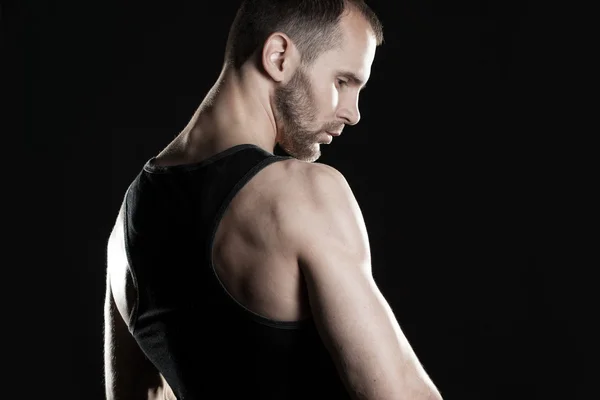 Muscular man,  clasps hands in  fist, black background, place for text on the right — Stock Photo, Image