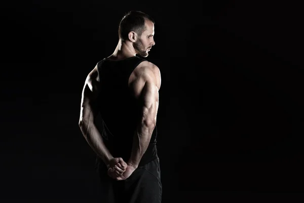 Muskulös man, knäppen händer i näven, svart bakgrund, plats för text till höger — Stockfoto