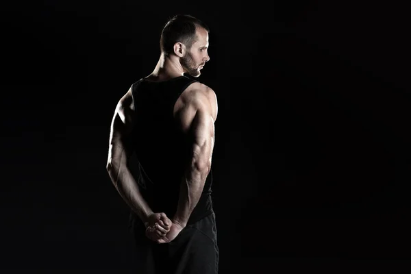 Muscular man,  clasps hands in  fist, black background, place for text on the right — Stock Photo, Image