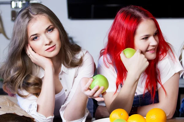 Twee jonge meisjes in de keuken praten en eten van fruit, gezonde levensstijl — Stockfoto