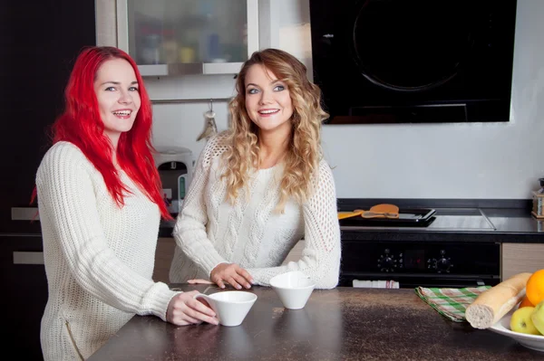Две молодые девушки на кухне говорят и едят фрукты, здоровый образ жизни — стоковое фото