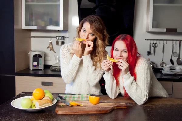 Две молодые девушки на кухне говорят и едят фрукты, здоровый образ жизни — стоковое фото