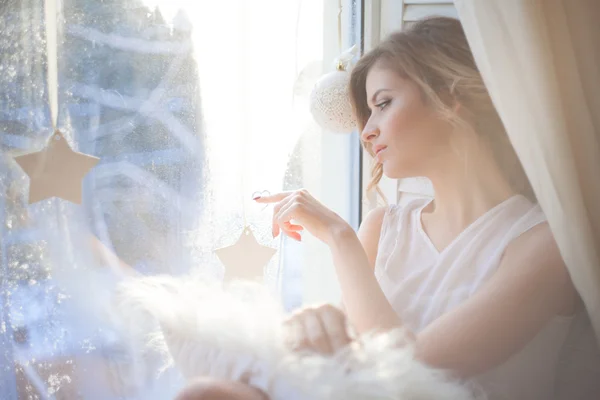 Hermosa mujer con maquillaje diario fresco y romántico peinado ondulado, sentado en el alféizar de la ventana, dibuja en vidrio —  Fotos de Stock