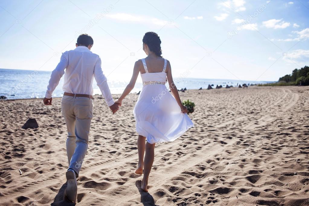 Just married happy couple running on a sandy beach, view from the back