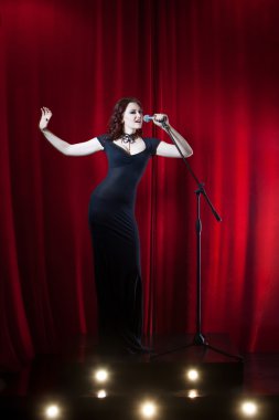 Sahne Alanı'nda güzel şarkı söyleyen kız. Güzellik kadını mikrofon ile. Kırmızı perde arka plan