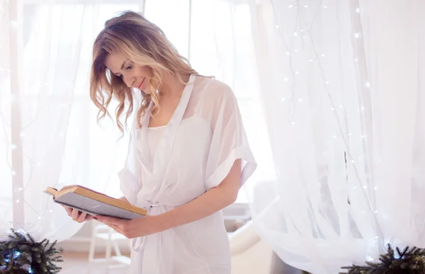Uma mulher lê um livro sentado na cama. Jovem menina bonita em seu quarto — Fotografia de Stock