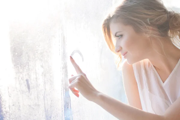 Taze günlük makyaj ve romantik dalgalı saç modeli, pencere pervazı oturan güzel kadınla camına çizer — Stok fotoğraf