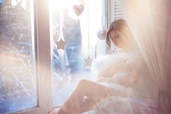 Hermosa mujer con maquillaje diario fresco y romántico peinado ondulado, sentado en el alféizar de la ventana, dibuja en vidrio —  Fotos de Stock