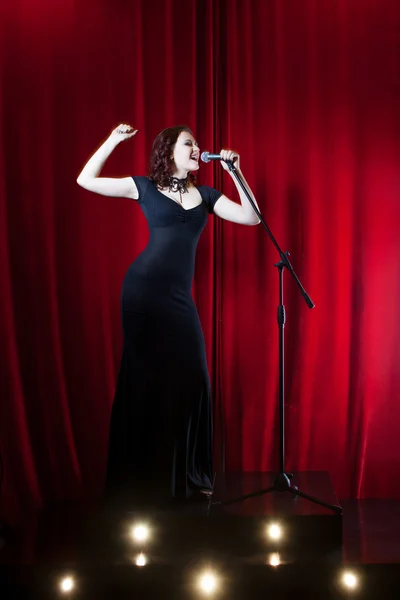 Bella ragazza che canta sul palco. Donna Bellezza con Microfono. sfondo tenda rossa — Foto Stock