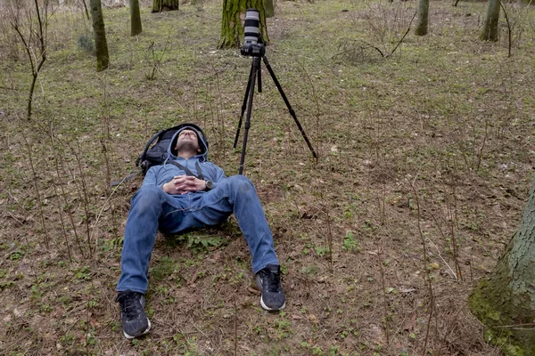 Fotógrafo está tirado en el suelo cerca de la cámara de pie y mirando a la distancia . —  Fotos de Stock