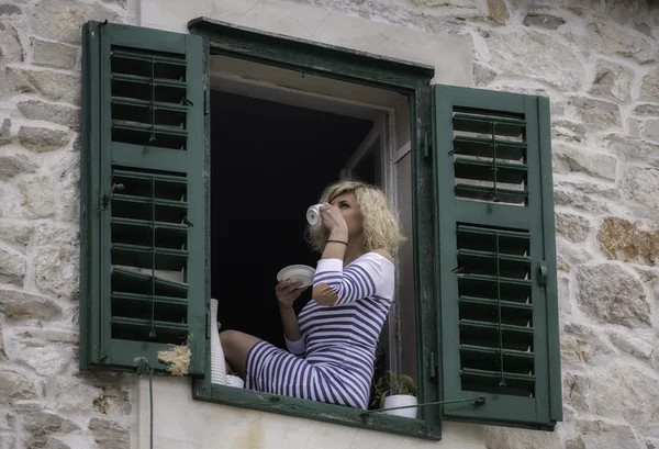 Hermosa mujer se sienta en el alféizar de la ventana y beber café —  Fotos de Stock