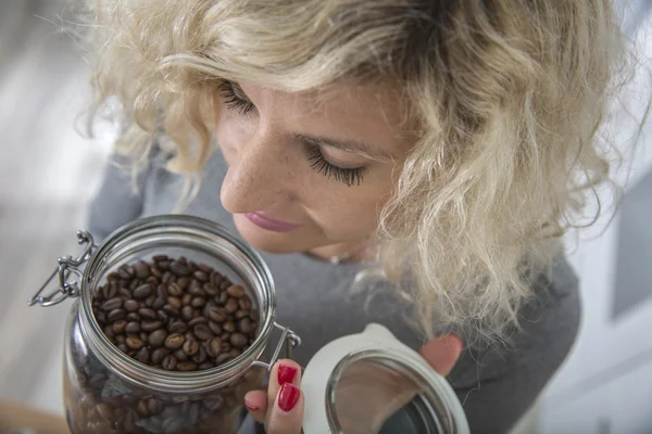 Chica rubia con el pelo rizado está oliendo granos de café en maceta de vidrio Imágenes De Stock Sin Royalties Gratis