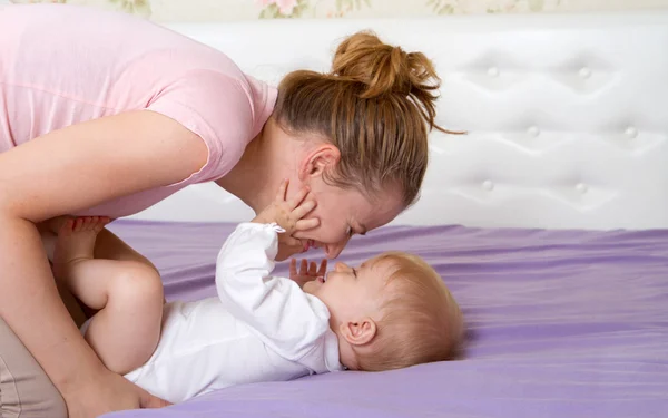 Mamma gioca con la bambina su un letto — Foto Stock