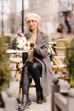 Bere takmış bir kadın ve terasta bir buket çiçekli bardaklar.