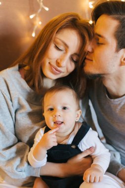 Çerçevede bir aile, anne ve baba kollarında bir kızla eğleniyorlar.