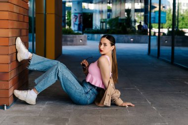 Genç çıplak ayaklı kız asfaltta oturuyor.